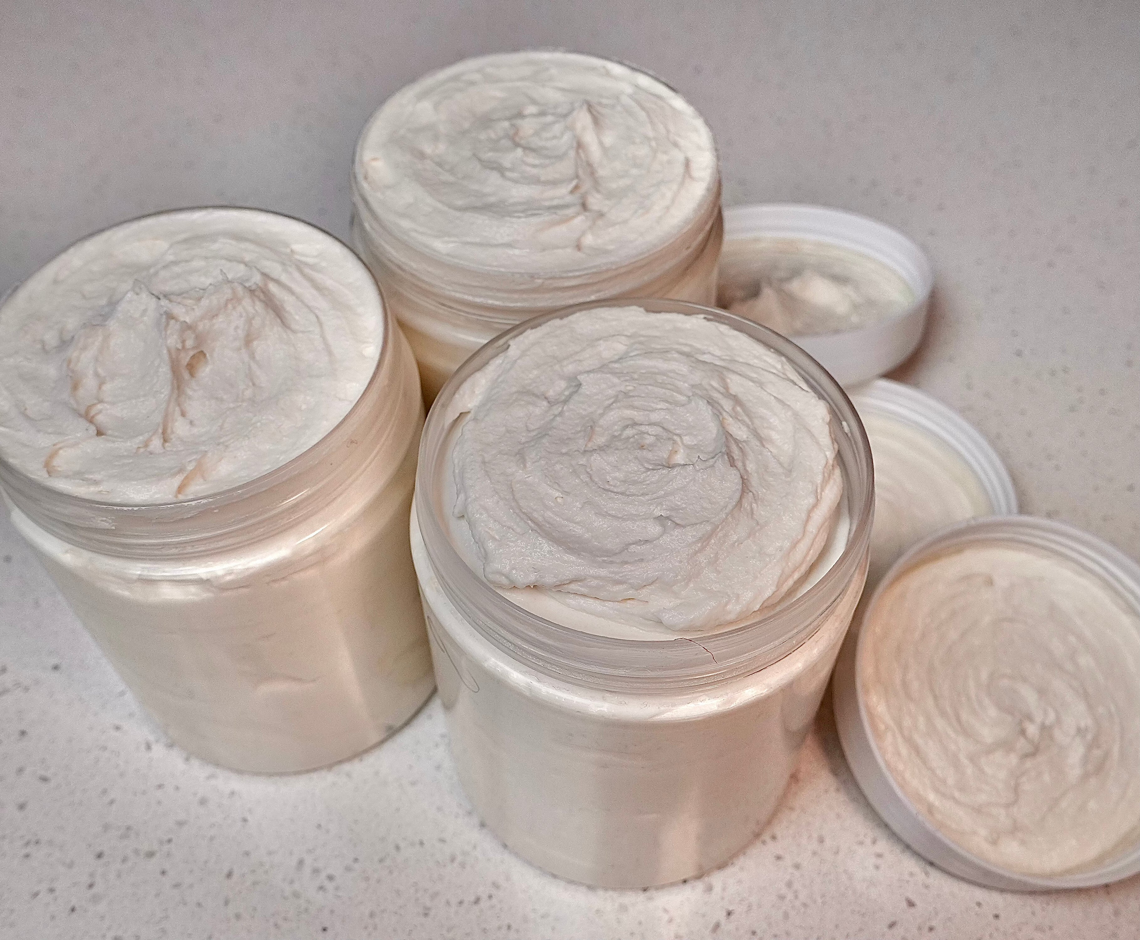 Three clear round jars filled with homemade white shea body butter, showcasing a luxurious skincare product for soft and radiant skin